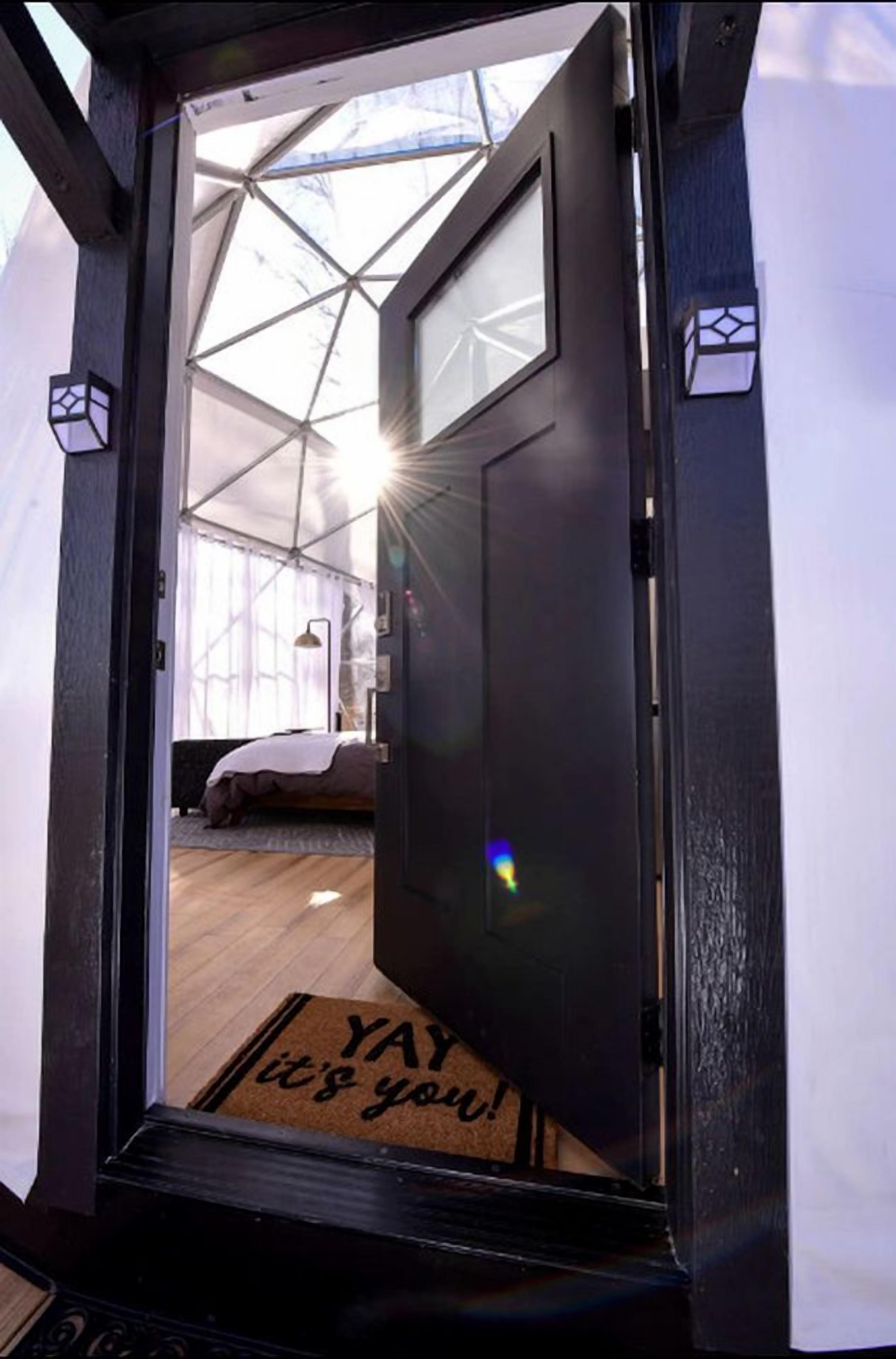 A door leading into a room with a bed, a lamp, and a window.