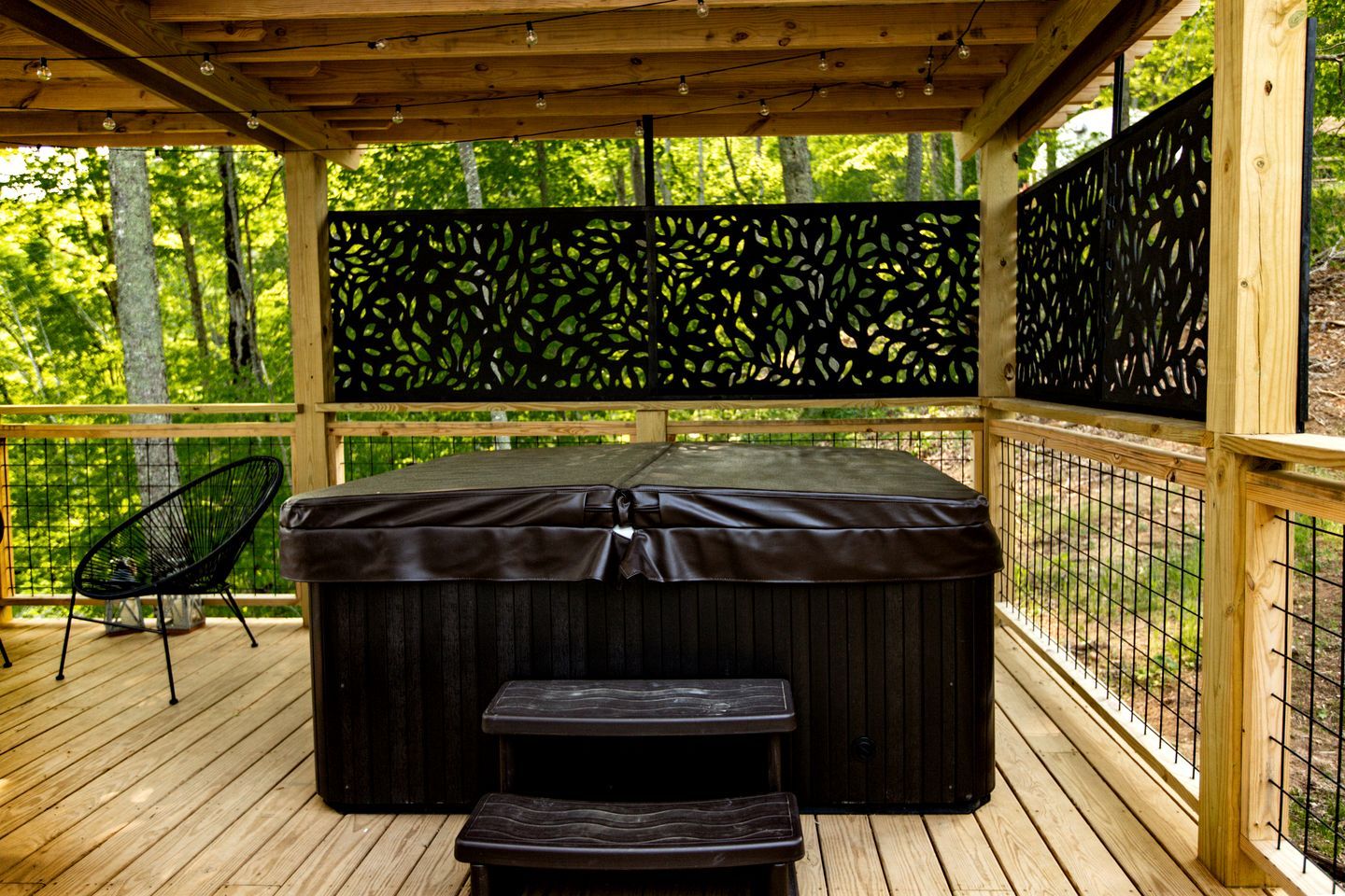 A wooden deck with a hot tub, a bench, and a chair.
