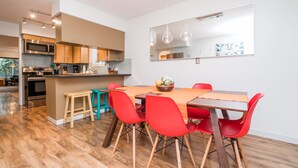 Eine moderne Küche mit Edelstahlgeräten, ein Essbereich mit roten Stühlen und einem Holztisch sowie ein großer Spiegel an der Wand.