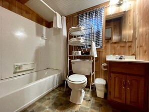 Un baño con inodoro y tina blancos, tocador de madera y barra de toallas de metal.