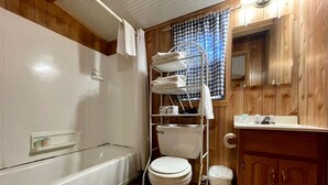 Ein Badezimmer mit Toilette, Badewanne, Waschtisch aus Holz und einem Handtuchhalter aus Metall.
