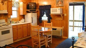 Ein Interieur einer Holzhütte mit Holzwänden, einer Küchenzeile inklusive Herd und Kühlschrank sowie einem Esstisch mit Stühlen.