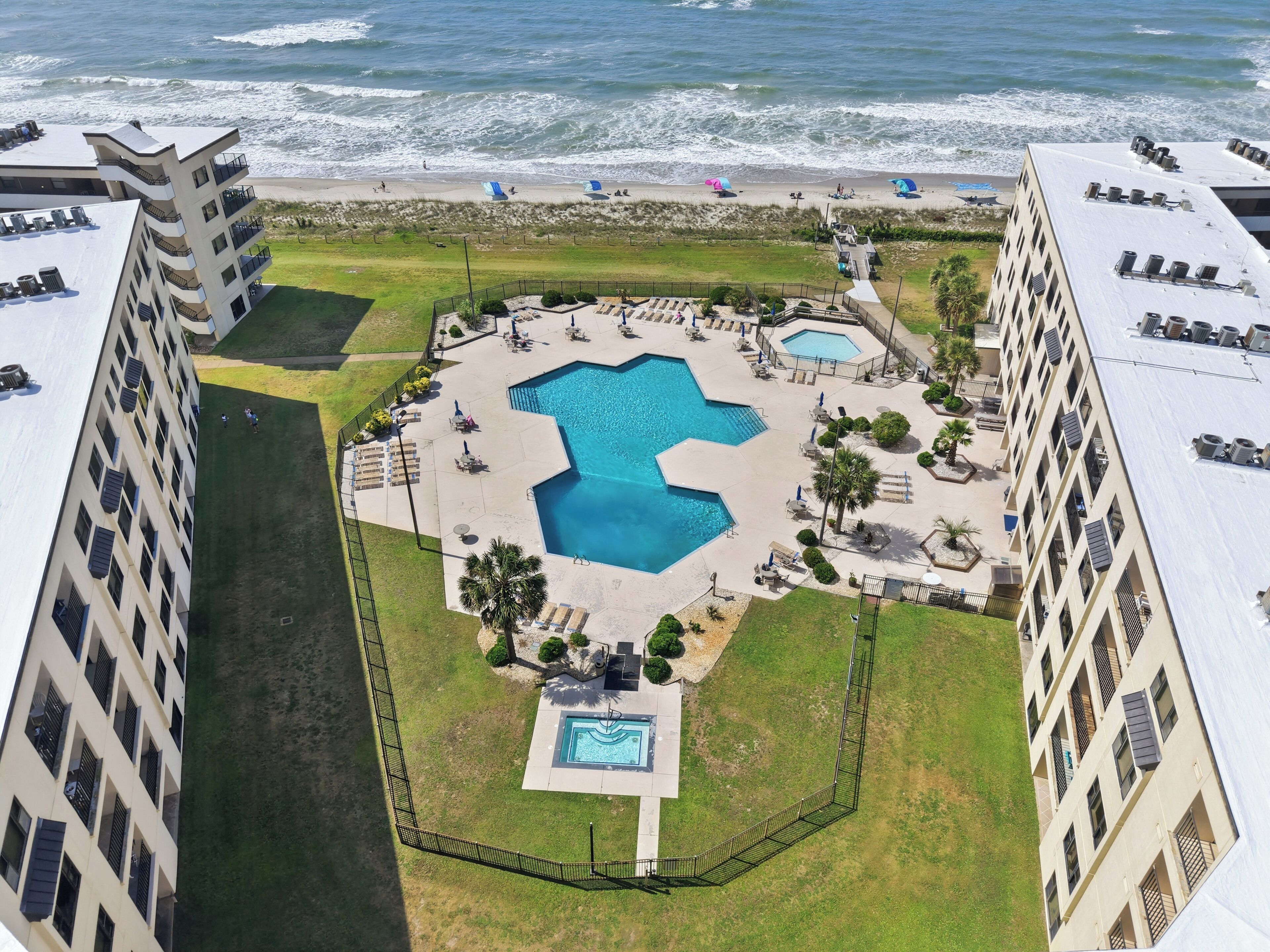 A hotel with a central swimming pool, multiple balconies, and a view of the ocean.