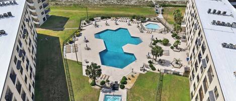 A hotel with a central swimming pool, multiple balconies, and a view of the ocean.