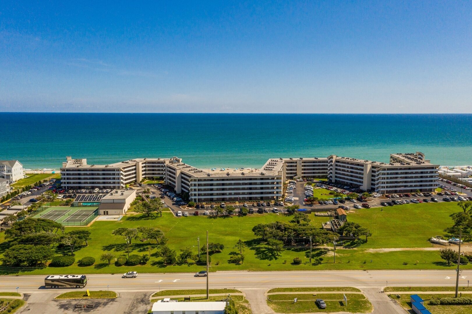 A coastal hotel with multiple buildings, a parking lot, and a tennis court.