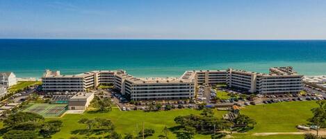 A coastal hotel with multiple buildings, a parking lot, and a tennis court.