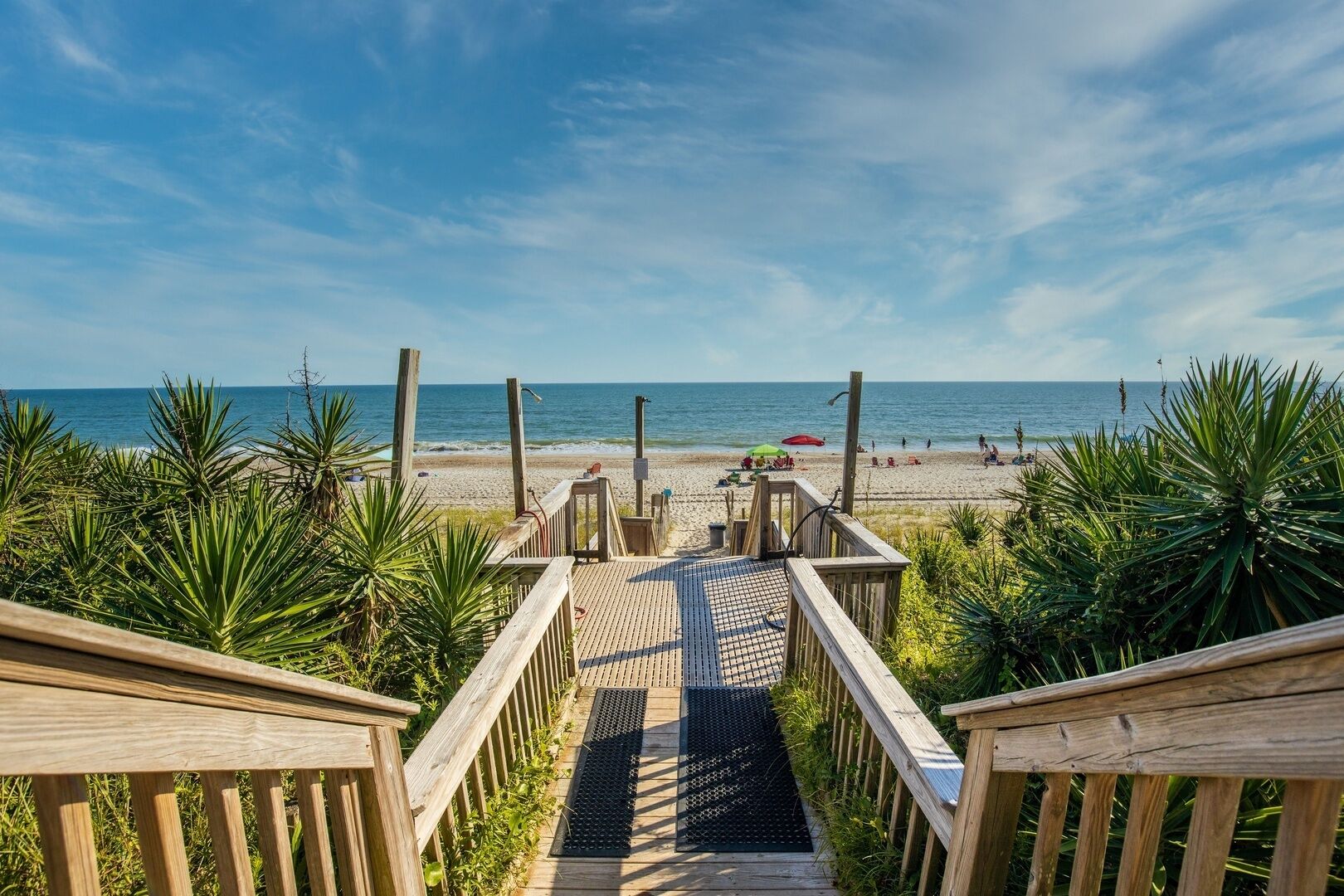 Een houten looppad dat naar een strand leidt, met palmbomen en een heldere lucht.