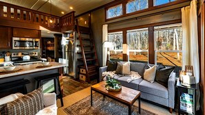 Ein gemütliches Wohnzimmer mit einer Couch, einem Couchtisch und Blick ins Freie durch große Fenster.