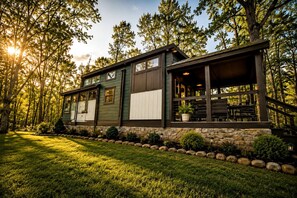 A two-story house with a stone foundation, a covered porch, and a well-maintained lawn. - Peaceful Pine Tiny House Retreat near South Cumberland State Park, Monteagle, TN (Monteagle)