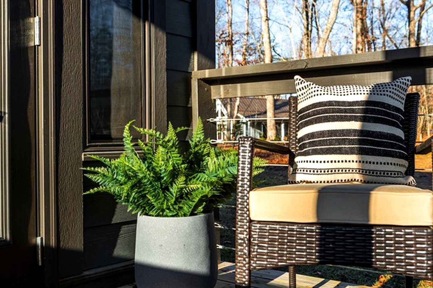 A wicker chair with a cushion and a striped pillow on a deck, next to a potted plant.