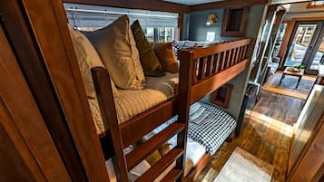 A bunk bed with wooden railings, a checkered pillow, and a window with blinds.