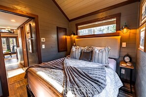 A bedroom with a bed, bedside tables, a window, and a door leading to an outdoor area. - Peaceful Pine Tiny House Retreat near South Cumberland State Park, Monteagle, TN (Monteagle)