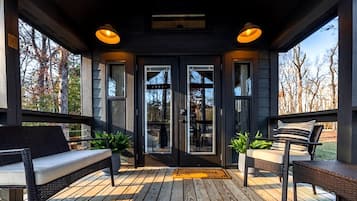 A covered porch with a bench, a door with glass panels, and a view of trees.