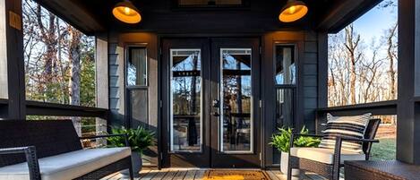 A covered porch with a bench, a door with glass panels, and a view of trees.