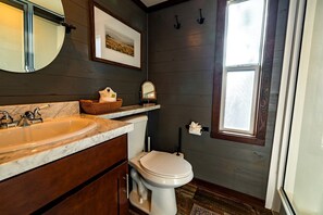 Ein Badezimmer mit Marmorwaschbecken, Holzschrankwaschbecken, Toilette, gerahmtem Bild an der Wand und einem Fenster.