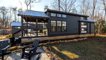 A modern cabin with a covered patio, outdoor seating, and a stone border.
