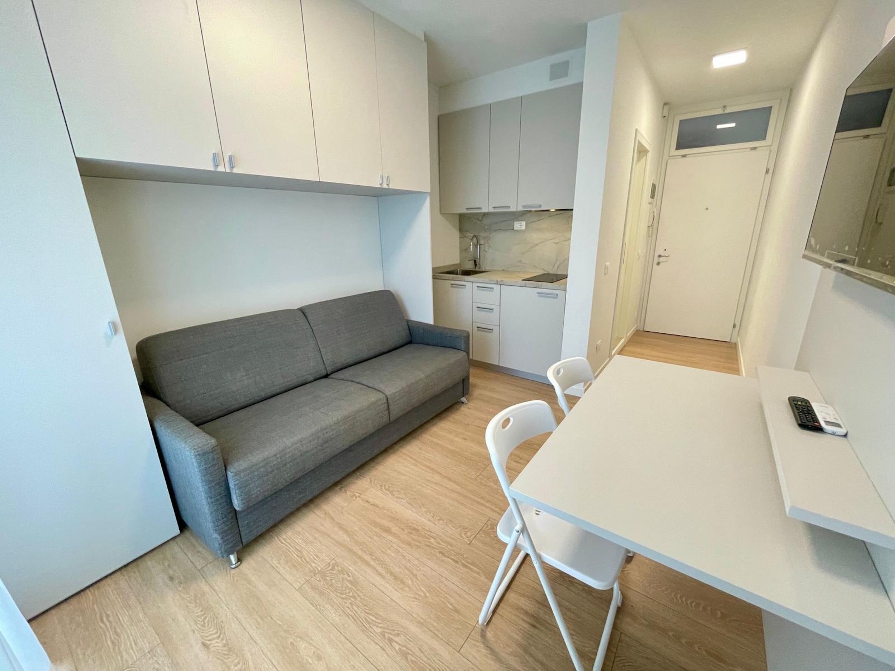 A compact living space with a sofa, a dining table, chairs, a kitchen area, and cabinets.