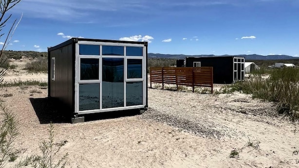 A small, modern building with a large windowed front, a bench, and a dirt ground. - Unique Mirror Pod on the Shores of Yuba Lake for a Fantastic Couples Escape in Utah (Levan)