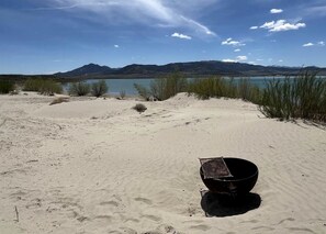 A desert landscape with a large body of water, mountains in the distance, and a black bowl on the sand.