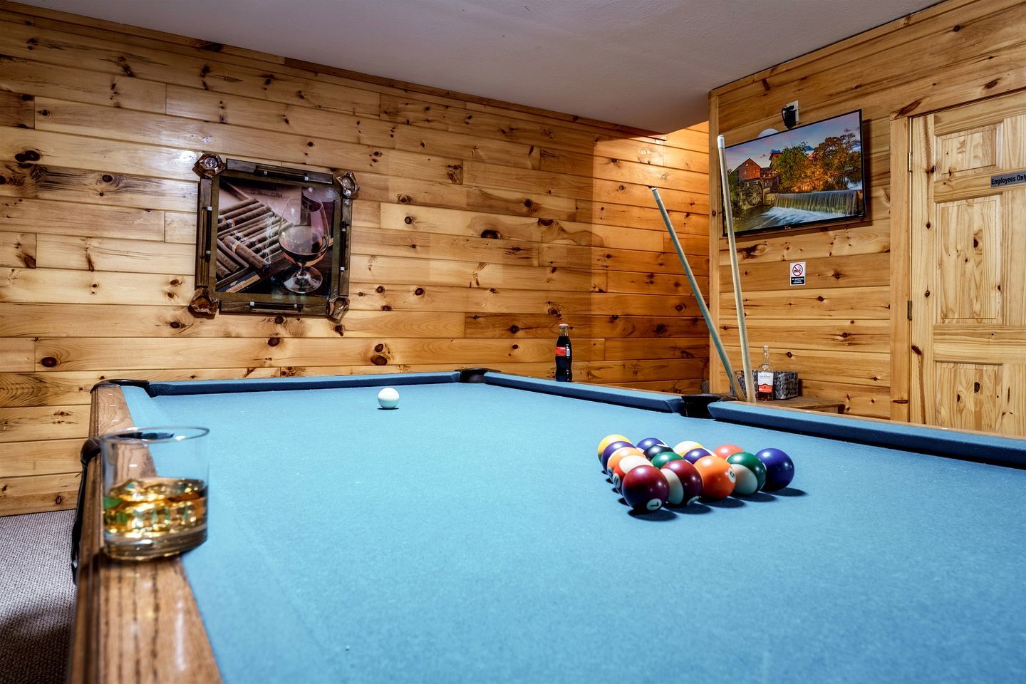 A pool table with balls, a framed picture, and a television on the wall.
