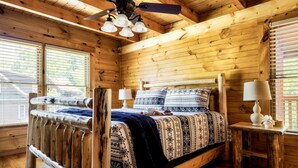 A wooden cabin bedroom with a bed, two bedside tables, a ceiling fan, and large windows. - Spectacular Cabin Surrounded by Trees in Pigeon Forge, Tennessee (Pigeon Forge)