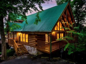 Eine Blockhütte mit einem grünen Dach, einer Holzwand und einer Veranda mit Stufen zum Eingang.