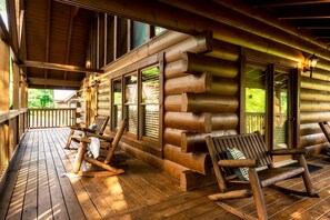 Eine Blockhütte mit einer Holzterrasse, großen Fenstern und einer Veranda mit Sitzgelegenheiten.