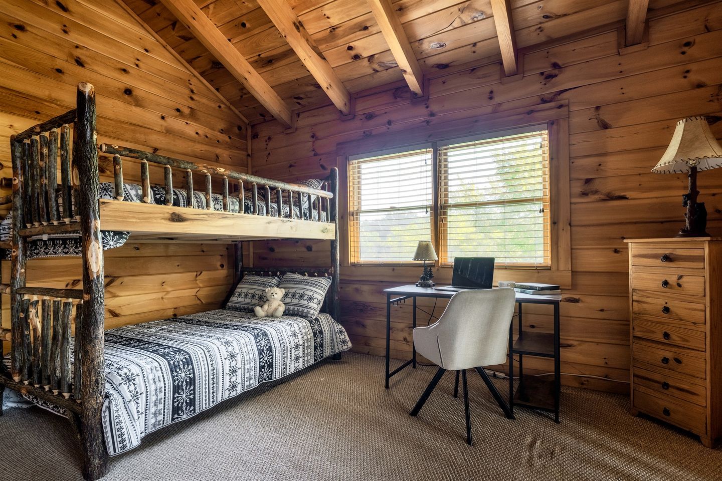 A cabin interior with a bunk bed, a desk with a computer, and a chair.