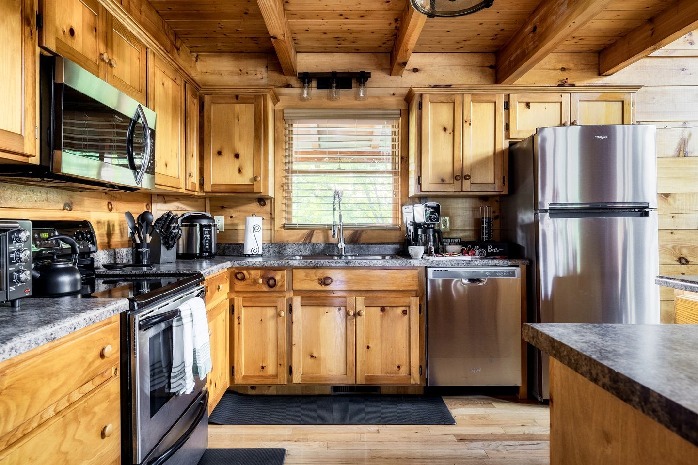 A wooden cabin-style kitchen with a built-in oven, microwave, coffee maker, and stainless steel refrigerator.