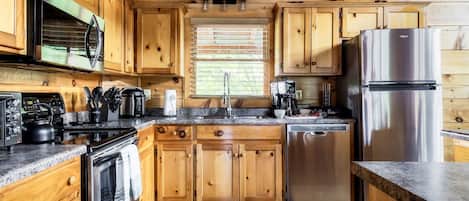 Una cocina tipo cabaña de madera con horno empotrado, microondas, cafetera y refrigerador de acero inoxidable.