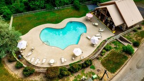 An aerial view of a swimming pool with lounge chairs and umbrellas, surrounded by greenery and a building with a sloped roof. - Spectacular Cabin Surrounded by Trees in Pigeon Forge, Tennessee (Pigeon Forge)
