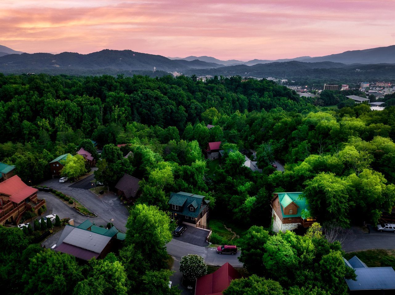 Quartiere residenziale con case immerse nel verde, strade e montagne sullo sfondo.