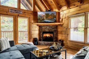 Ein Cabin-Innenraum mit Kamin aus Stein, einem darüber hängenden Fernseher und einer gemütlichen Sitzecke mit Sofa und Couchtisch.