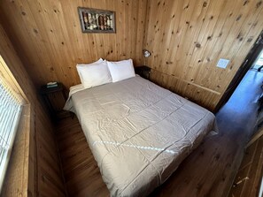 Una habitación con paneles de madera, una cama, una mesita de noche y un reloj en la pared.
