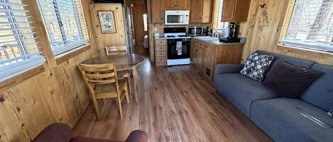 A wooden cabin interior with a dining area, kitchenette, and seating area.