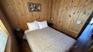 Ein Zimmer mit Holzwänden, einem Bett, einem Nachttisch und einer Wanduhr.