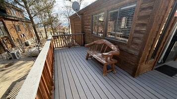 Una terraza de madera con un banco, una antena parabólica y un edificio con ventanas amplias.
