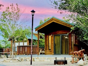 A wooden cabin with a porch, a stone wall, and a wooden deck.