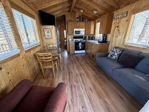 Interior de una cabaña de madera con comedor, kitchenette y zona de estar.