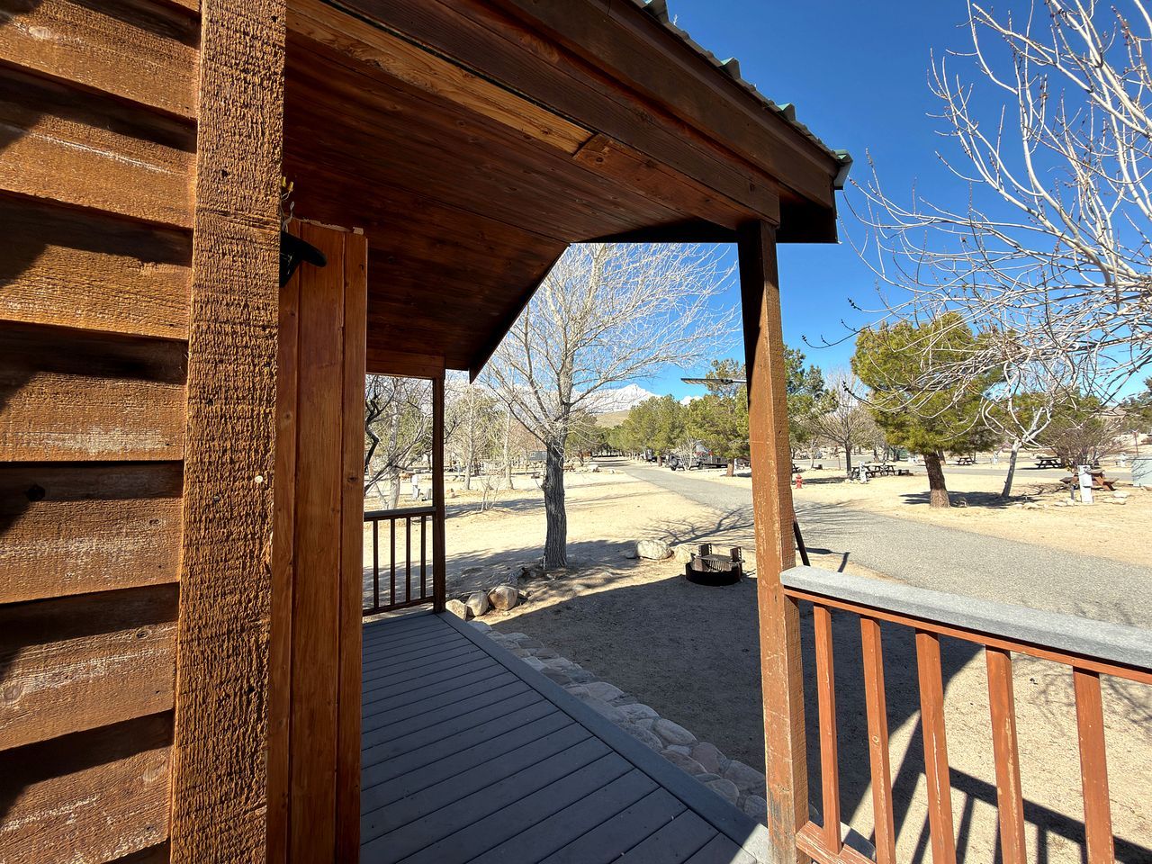A wooden deck with a railing, a clear sky, and a view of a park with trees and a bench.