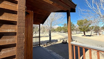 A wooden deck with a railing, a clear sky, and a view of a park with trees and a bench.