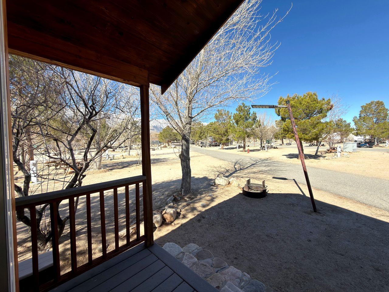 A covered outdoor area with a wooden deck, a stone pathway, and a view of a road and trees.