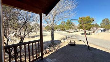 A covered outdoor area with a wooden deck, a stone pathway, and a view of a road and trees.