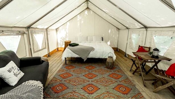A tented accommodation with a bed, a table, and a couch.