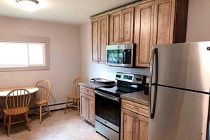 A kitchen with wooden cabinets, a stainless steel refrigerator, a microwave, and an oven. There is a dining table with chairs.