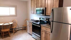 Une cuisine avec des meubles en bois, un réfrigérateur en acier inoxydable, un four à micro-ondes et un four traditionnel. On y trouve également une table à manger avec des chaises.