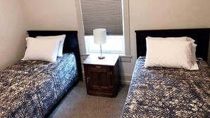 Une chambre avec deux lits, une table de chevet et une fenêtre avec des stores.