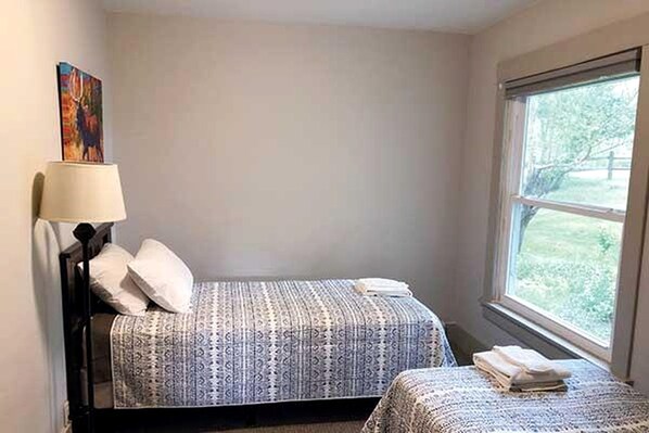 A bedroom with two beds, a window, and a painting on the wall.
