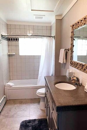 Une salle de bain équipée d’une baignoire, de toilettes, d’un lavabo et d’un miroir agrémenté d’un cadre décoratif.