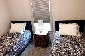 Une chambre avec deux lits, une table de chevet et une fenêtre avec des stores.
